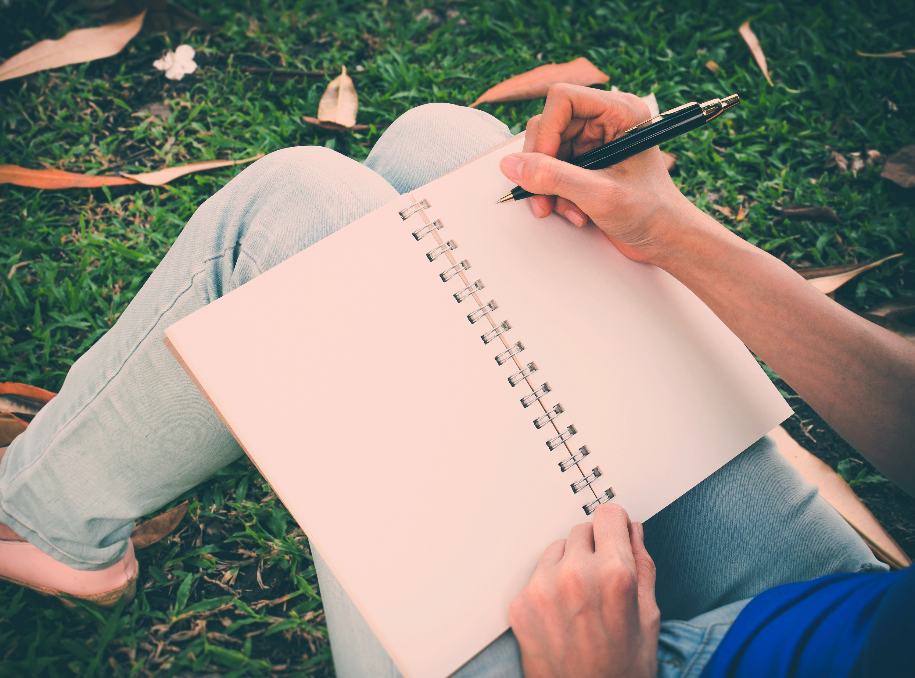 Close-up of someone writing in a notebook in a sunny park