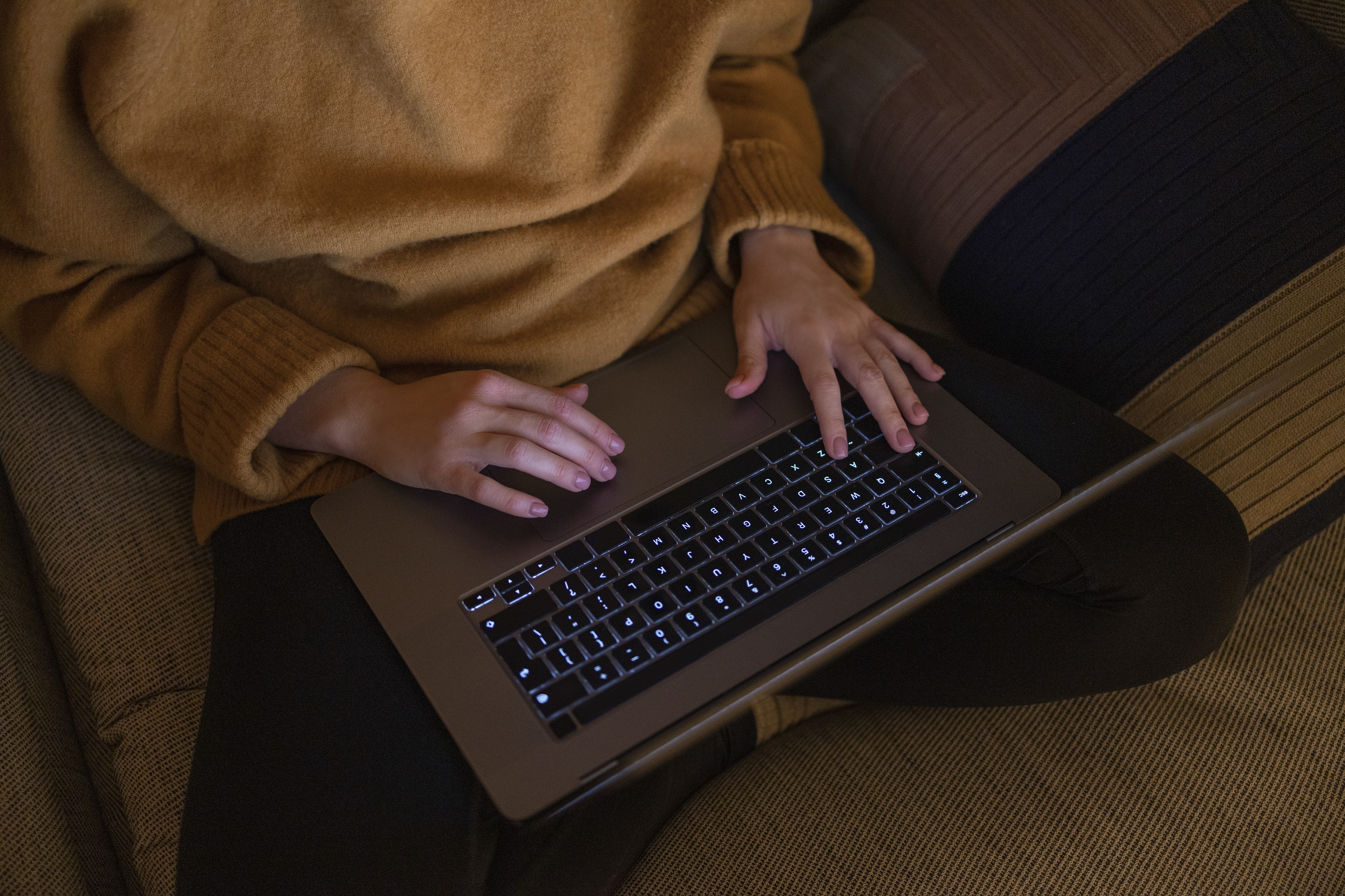 Woman in yellow jumper writing with her laptop on her lap, late at night